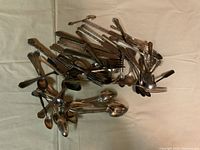 Top view of a mixed pile of various silverware utensils including forks, knives, and spoons on a neutral background.