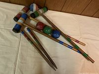 Overview photo of croquet mallets and balls on a beige cloth background.