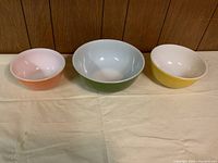 Three vintage Pyrex bowls in peach, green, and yellow colors arranged side by side.
