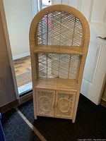 Front view of the white wicker shelving unit showing two shelves and cabinet doors with sunburst wicker patterns.