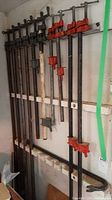 Wide view of ten bar clamps hanging on a rack