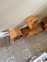 Photo showing five small wooden bird houses placed on a tiled floor, varying slightly in design and size.