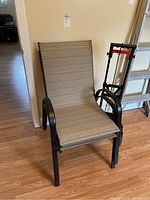 Two beige outdoor chairs with metal frames and a folded moving cart beside them on wood flooring.