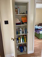 Closed closet with shelves holding folded towels, cleaning bottles, and assorted items.