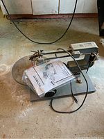 Front‐left view of saw on basement floor showing tabletop, motor housing, power cord and manual on table