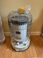 Front view of the kerosene heater showing its cylindrical body, metal cage, control knob, and push-to-light button with the funnel bag resting on top.