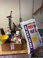 Overview of wooden box with assorted household supplies and large bag of Sela Ice Salt