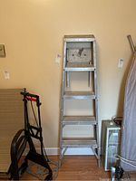 Full view of aluminum step ladder from front showing four steps and top platform with surrounding items for scale.