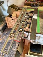 Three metal framed bubble levels and a flat metal measuring tool arranged on a workbench showing overall lot