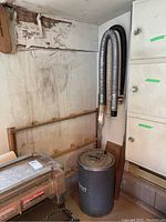 Rockwell vacuum cleaner unit with attached hoses in a corner next to cabinetry and a workbench.