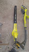 Ryobi yellow and black cordless hybrid weed eater and leaf blower, cordless weed eater, two batteries, and charger on concrete floor