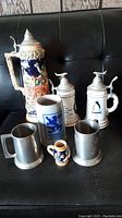 Group view of seven assorted steins and tankards on black surface