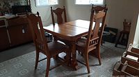 Full view of solid wood dining table set with four chairs and window background