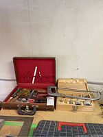 Photo showing the wooden toolbox with red felt lining holding screwdrivers and hand tools, the hand saw, and wooden box with drill bits and clamp.