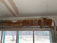Wide view of large collection of wooden bar clamps hanging from a beam, showing entire set and dust accumulation.