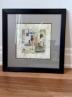 Framed abstract print artwork on beige wall and hardwood floor background.