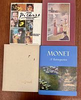 Top view showing 4 books stacked with distinct covers for Picasso, Seurat, Monet, and a beige hardcover book.