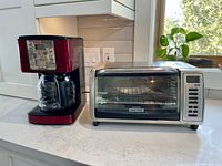 Sunbeam coffee maker and Black+Decker toaster oven side by side on kitchen counter near window