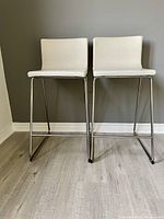 Front view of two cream leather stools showing seat and base design