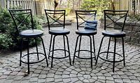 Four black metal barstools arranged in a row outdoors on a paved surface.