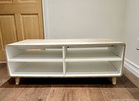 Front view of the coffee table showing the white shelving interior with removable adjustable shelves and light wood tone frame with curved edges.