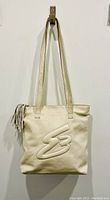 Front view of cream leather tote bag showing embossed 'SB' logo and tassel on the zip pull.
