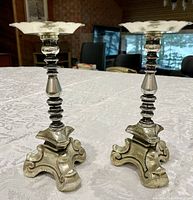 Pair of vintage brass candlesticks on white patterned tablecloth with interior room background visible.