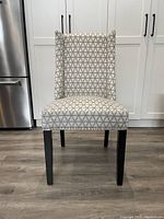 Front view of wingback chair with grey and white geometric patterned upholstery, black legs, and nailhead trim.