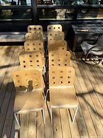 Overview photo showing 10 Ikea Jules dining chairs arranged outdoors, plywood seats and backs with circular cut-outs, white metal legs.