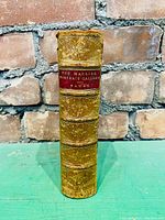 Photo showing the spine of the leather bound book with gold tooling and red labeled title.