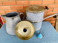 Photo of the antique double boiler with bronze-colored lid, large enamelware kettle, and blue funnel, showing details and condition.