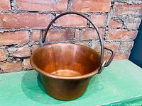 Front side photo showing the copper pot against a brick wall on a green surface, highlighting the wide opening and inside of pot.