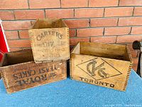 Three wooden advertising crates stacked and aligned showing logos and printed text on their sides.