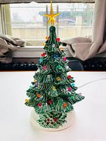 Front view of small green ceramic Christmas tree with multi-colored lights and yellow star topper on white base.