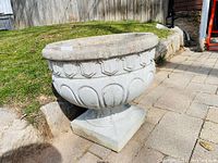 Side view of large cast concrete Roman-style planter urn on stone patio and grass