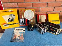 Vintage Kodak Brownie and movie camera accessories including flash outfit, boxes, and manuals on display against brick background