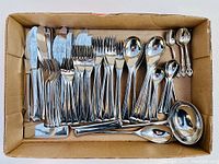 Top view of the entire flatware set in a box showing knives, forks, multiple spoon sizes and serving utensils arranged neatly.