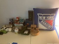 Full lot overview showing NY Rangers pillow, wooden music box car, bobblehead dog basketball figure, baseballs, ship in bottle, metal bank, VHS tapes, and small toy cars.