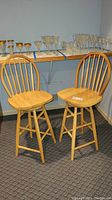 Pair of wooden swivel high back bar stools with light wood finish in a room next to a shelf of glassware