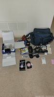 Photo showing entire lot including cameras, lenses, camera bag, and accessories arranged on floor.