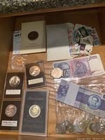 Overview of lot showing proof coins in holders, belt buckle, banknotes, bag of foreign coins and stamps
