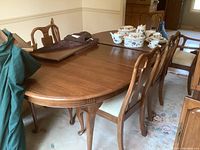 Photo showing walnut dining table set with table pads and tabletop items on surface, six chairs around table.