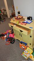 Wide view of assortment of games and toys on and around a green cabinet showing paddle balls, dominoes, Angry Birds game, water shooters, and wooden truck.
