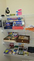 Shelving with multiple stacked board games including Monopoly, Sorry, Scattergories, Anybody's Game, and Tiddlywinks, packs of playing cards, and a travel blanket.