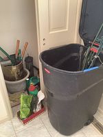 View of the Rubbermaid black lidded trash can, planters, hand tools and gardening supplies.
