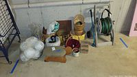 Wide view of lot showing hose reel, baskets, white soccer ball, stools, and other miscellaneous items on a basement floor.