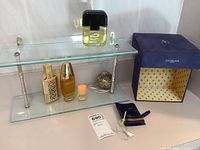 Glass shelf holding various perfume bottles including Avon and Estee Lauder, decorative bottle, orange vial, and Guerlain box nearby.
