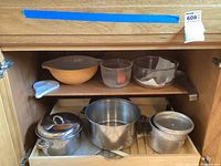 Wood cabinet shelf with vintage Pyrex bowls, glass bowls, blue plastic divided tray, metal pots and colander.