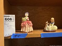 Two Royal Doulton porcelain figurines displayed on a wooden shelf; tallest approximately 5 inches tall