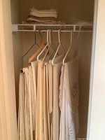 Stack of assorted neutral-colored linens and napkins hanging and folded on closet rod, showing various fabrics and sizes.